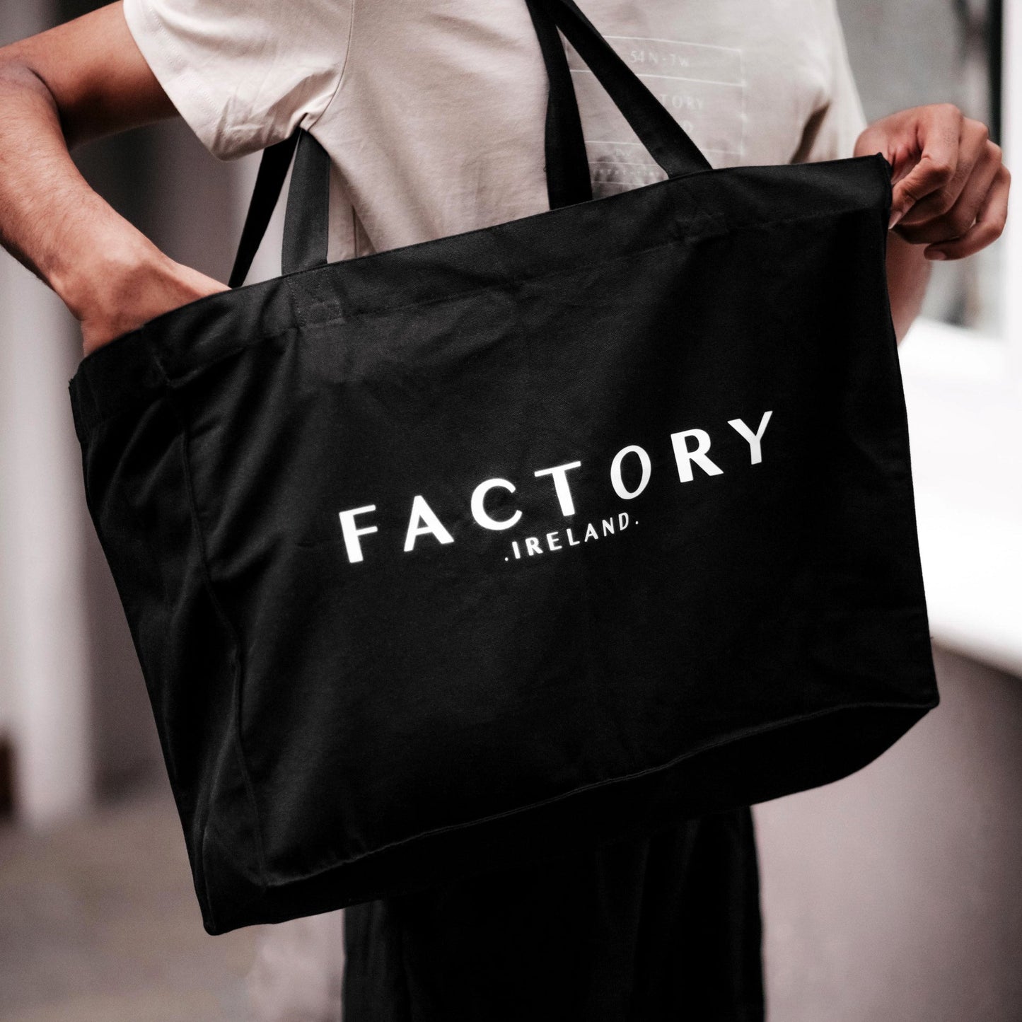 Person holding a black tote bag with 'Factory Ireland' text.