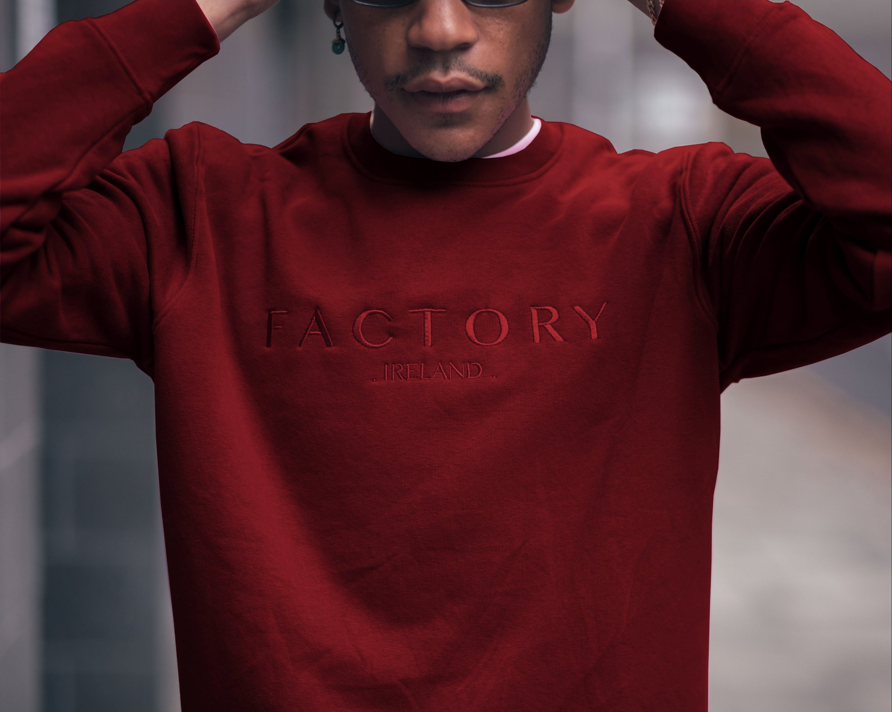 Person wearing a red sweatshirt with 'FACTORY IRELAND' branding against a blurred background