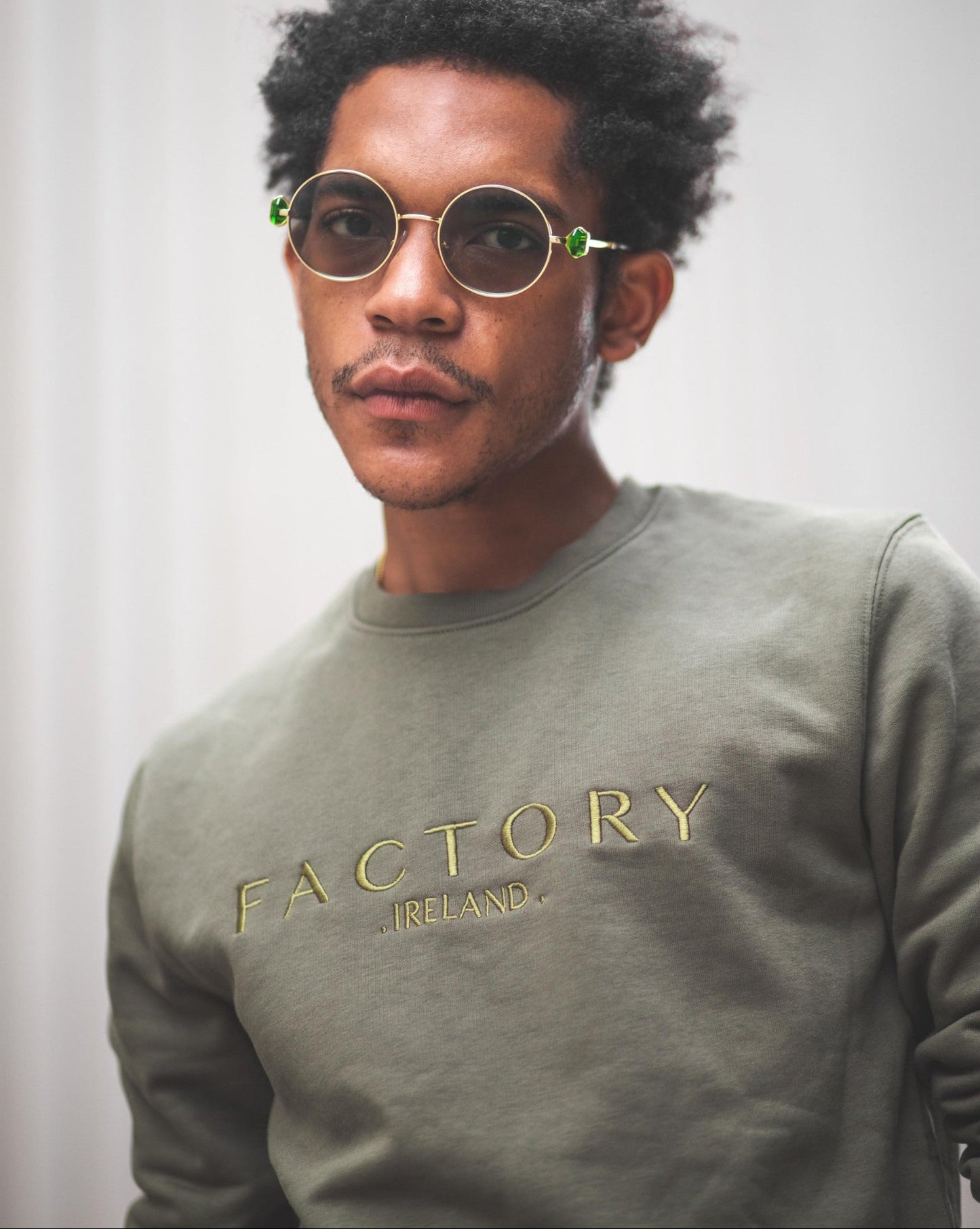 Person wearing a green 'Factory Ireland' sweatshirt with round sunglasses.