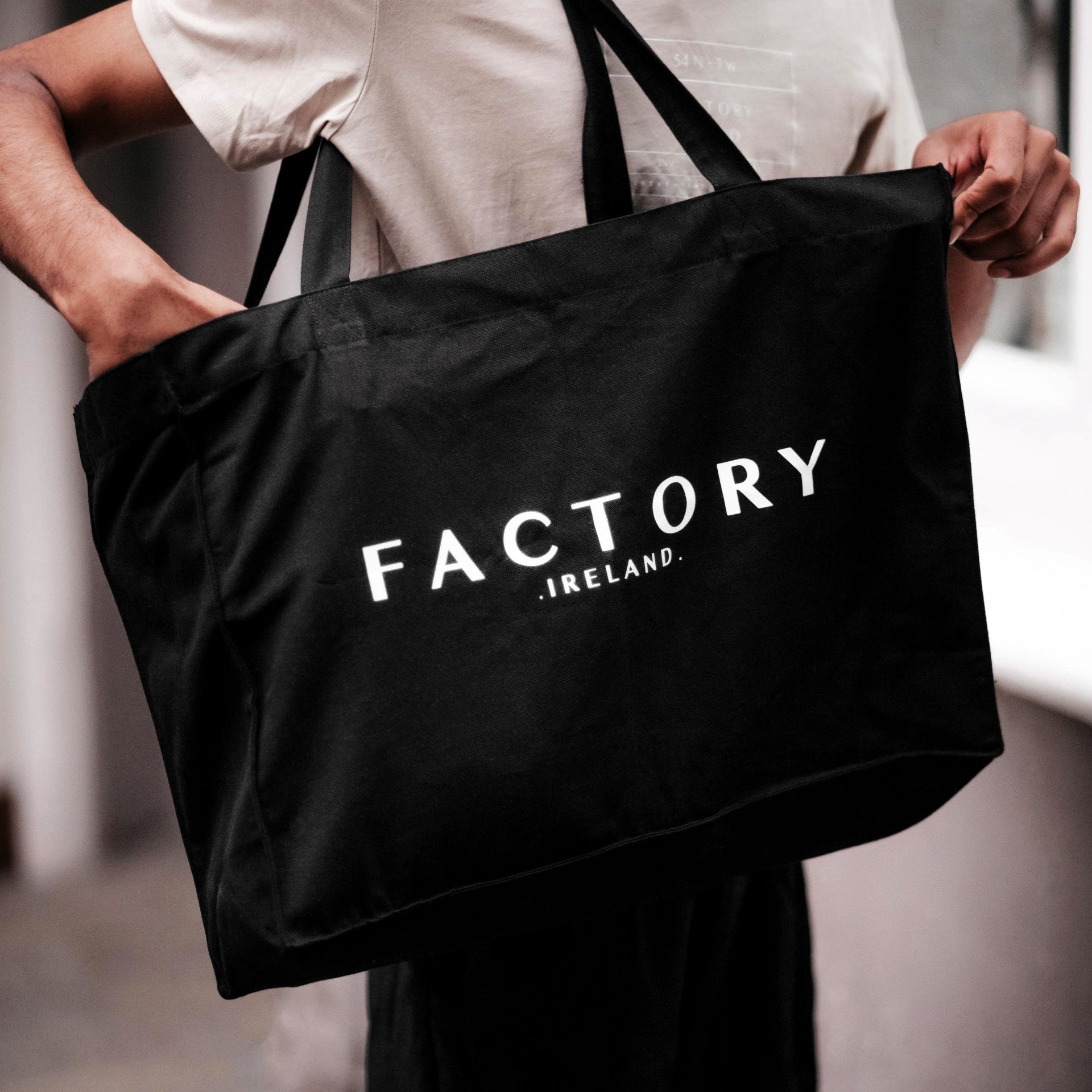 Person holding a black tote bag with 'Factory Ireland' text.
